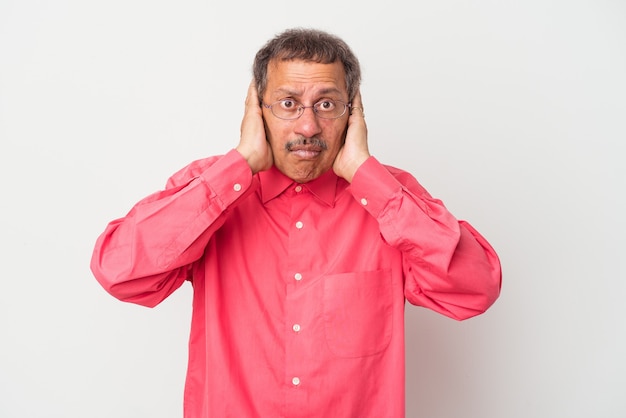 Middle aged indian man isolated on white background covering ears with hands trying not to hear too loud sound.