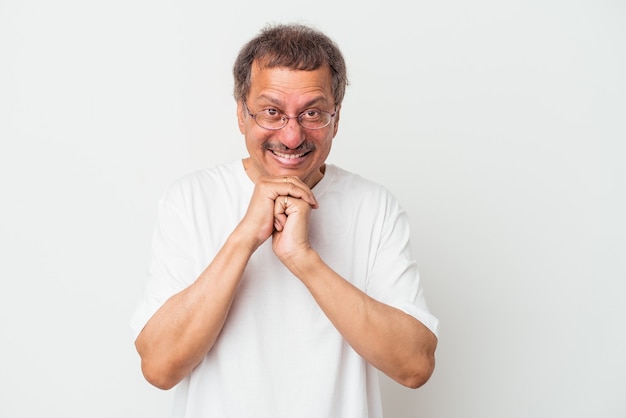 Middle aged indian man isolated on white background keeps hands under chin, is looking happily aside.