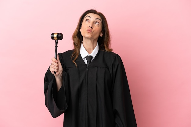 Middle aged judge woman isolated on pink background and looking up