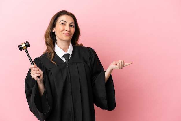 Middle aged judge woman isolated on pink background pointing finger to the side and presenting a product