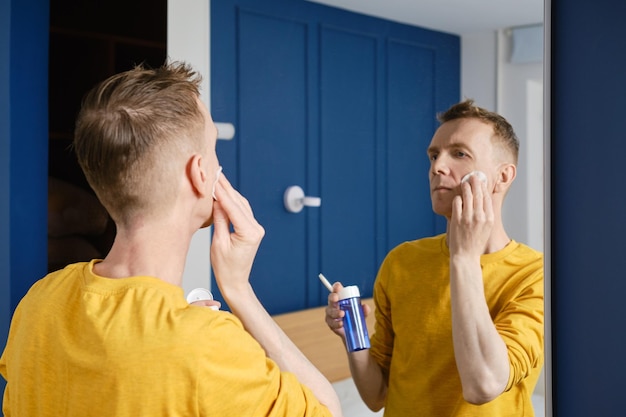 Middle aged man cleansing face with toner using cotton pad