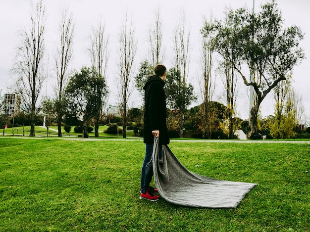 Middle aged man unfolding blanket in the park. Mental health concept. Isolation, loneliness, time alone, rituals and social distancing concept