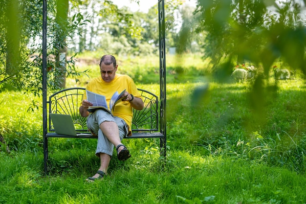 Middle aged man with laptop and documents working outside in garden green home office concept