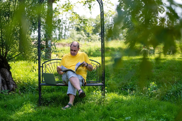 Middle aged man with laptop and documents working outside in garden green home office concept