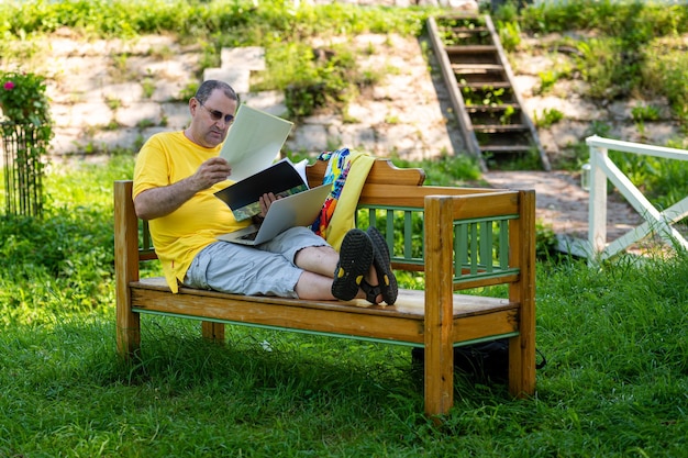 Middle aged man with laptop and documents working outside in garden green home office concept