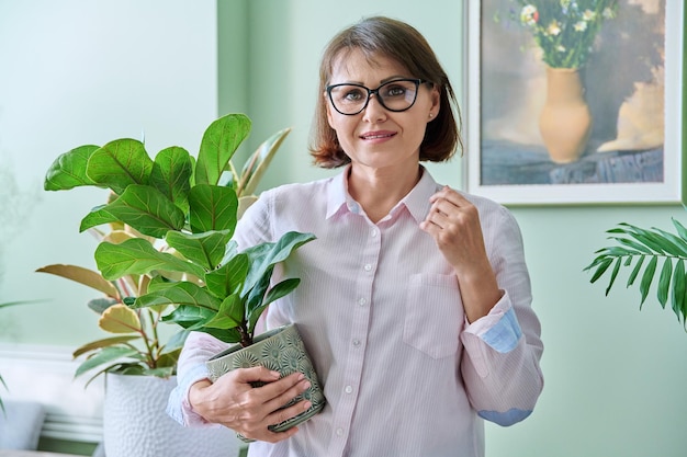 Middle aged smiling woman with potted plant at home