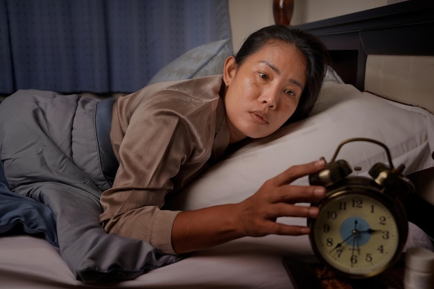 Middle aged woman depressed and stressed lying in bed looking at the clock from insomnia