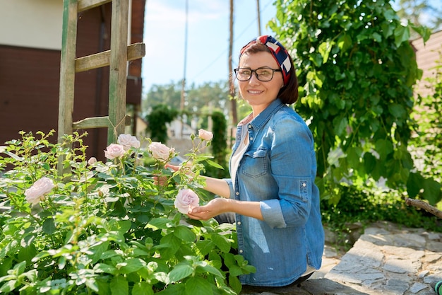 Middle aged woman enjoying beauty of rose bush spring nature