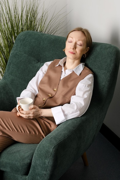 Middle aged woman having rest during coffee break in office recreation room