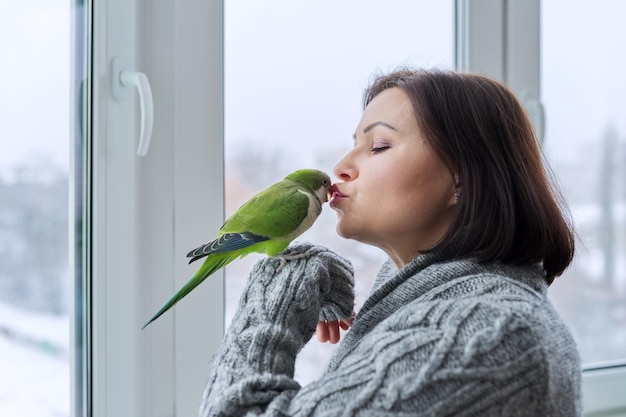 Middle aged woman and parrot together female bird owner talking kissing green quaker pet