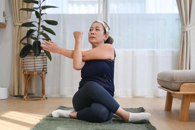 Middle aged woman in sport clothes sitting on the yoga mat and stretching her body Healthy lifestyle concept