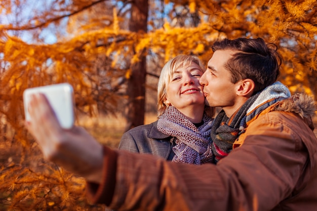 Middle aged woman taking selfie with her adult son using phone