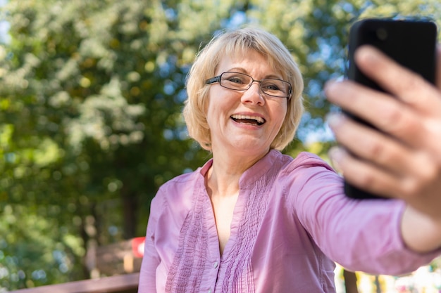 A middle-aged woman talking on the phone and taking a selfie . A woman communicates, blogging, checking e-mail. Social media, network.