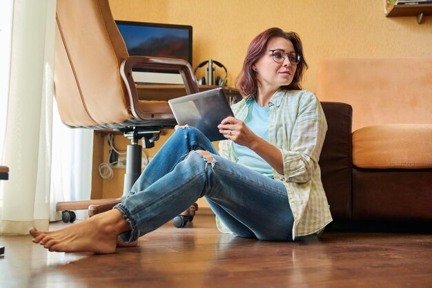 Middle aged woman with digital tablet home workplace with computer background