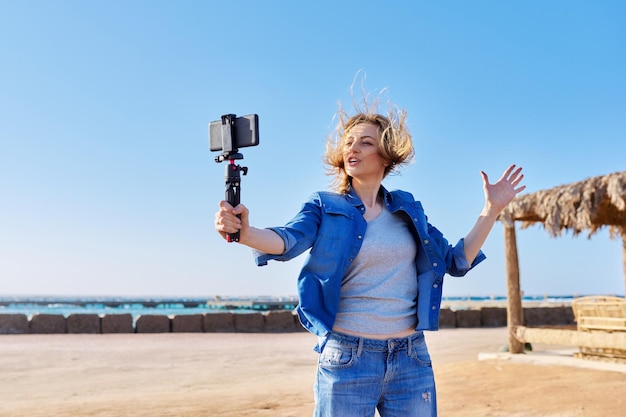 Middle aged woman with smartphone looking at webcam talking recording video