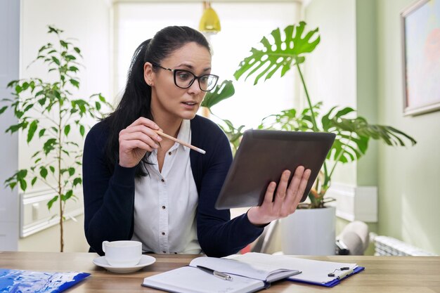 Middle aged woman working at home using digital tablet for video call conference