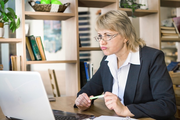 Middle-aged woman working on laptop in cafe, in office. She is very surprised. Remote work