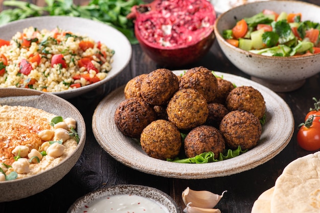 Middle eastern or arabic cuisines, falafel, hummus, tabouleh, pita and vegetables on wooden table, selective focus