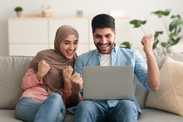 Middle eastern couple using laptop computer shaking fists at home