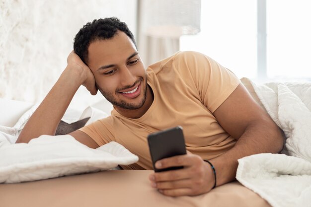 Middle eastern guy using cellphone and mobile application in bedroom