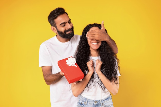 Middle eastern husband surprising wife with present closing eyes studio