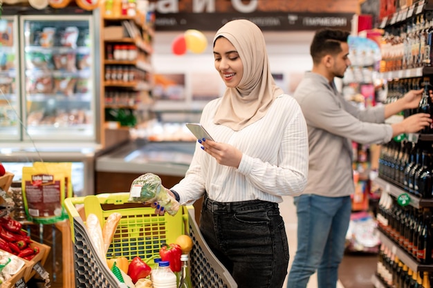 Middle eastern lady buyer shopping using cellphone in supermarket