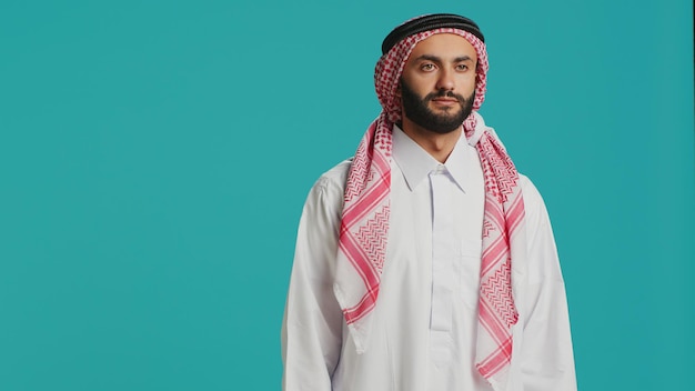 Middle eastern man in traditional attire smiling and posing with confidence representing arabic cultural identity with checkered print headscarf and white robe Young cheerful arab person