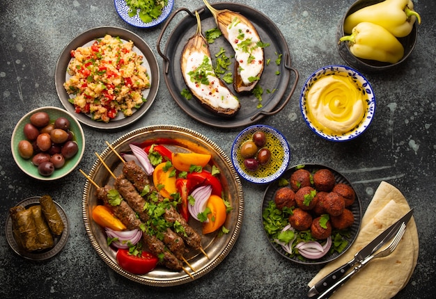 Middle eastern or Mediterranean dinner with grilled kebab, falafel, roasted and fresh vegetables, assorted Arabic meze and appetizers served on rustic background table. Dinner table overhead