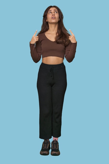 Middle Eastern woman full body studio pointing upside with opened mouth