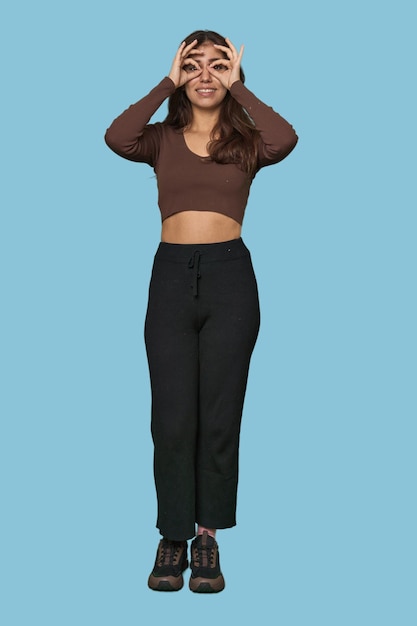 Middle Eastern woman full body studio showing okay sign over eyes