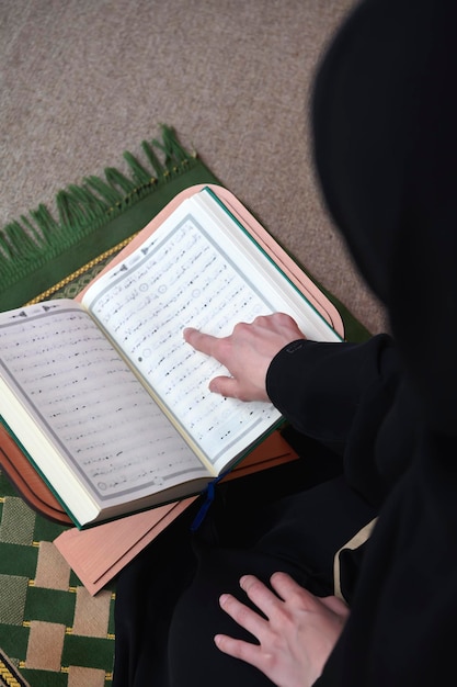 Photo middle eastern woman praying and reading the holy quran, public item of all muslims. education concept of muslim woman studying the holy quran at home or mosque in ramadan month.