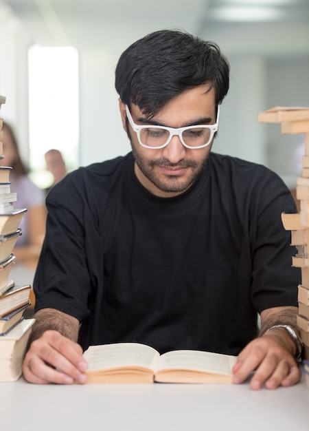 Middle eastern young student studying in college library with stack of books