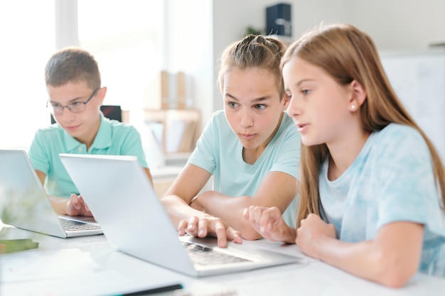 Middle school boy and girl sitting by desk in classroom and looking at curious stuff on laptop display at lesson