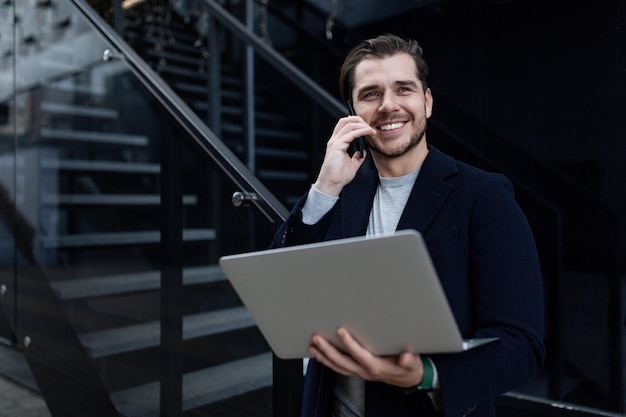 Middleaged business man speaks on a mobile phone with a wide smile and holds a laptop in his hands