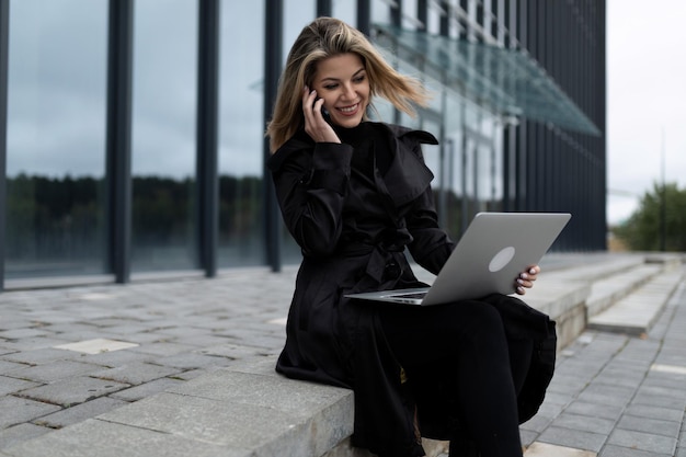 A middleaged businesswoman woman works online on a laptop against the backdrop of an office building