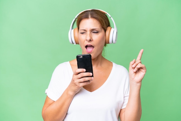 Middleaged caucasian woman over isolated background listening music with a mobile and singing