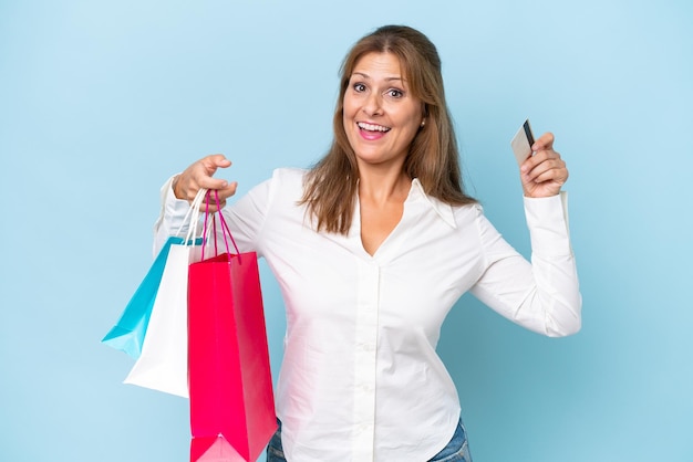 Middleaged caucasian woman isolated on blue background holding shopping bags and surprised