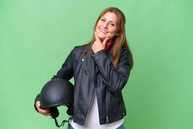 Middleaged caucasian woman with a motorcycle helmet over isolated background happy and smiling