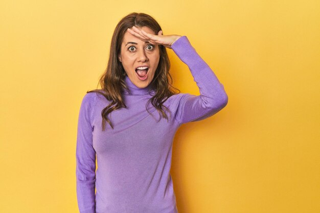 Photo middleaged caucasian woman on yellow shouts loud keeps eyes opened and hands tense