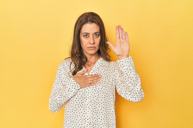 Middleaged caucasian woman on yellow taking an oath putting hand on chest