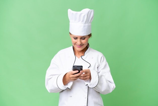 Middleaged chef woman over isolated background sending a message with the mobile