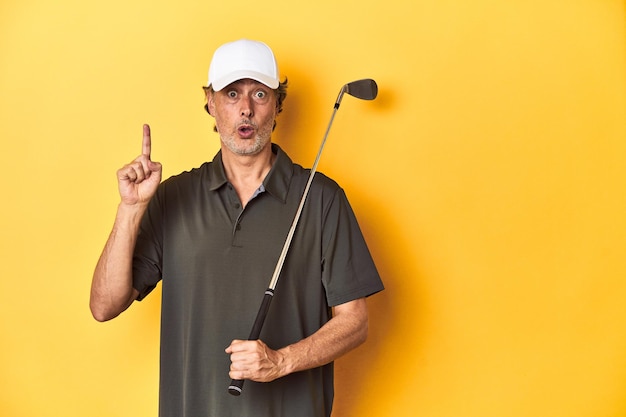 Middleaged golfer with club and cap on yellow having some great idea concept of creativity