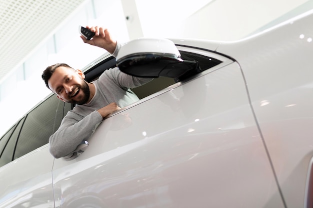 Middleaged man looking out of the car showing the keys of the newly purchased car