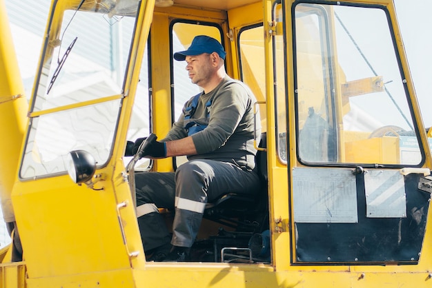 Middleaged man sits in cab of tractor and works Portrait of worker in open cab of truck tractor or loader Authentic summer day workflow