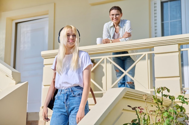 Middleaged mother seeing off her teenage daughter on the porch of the house