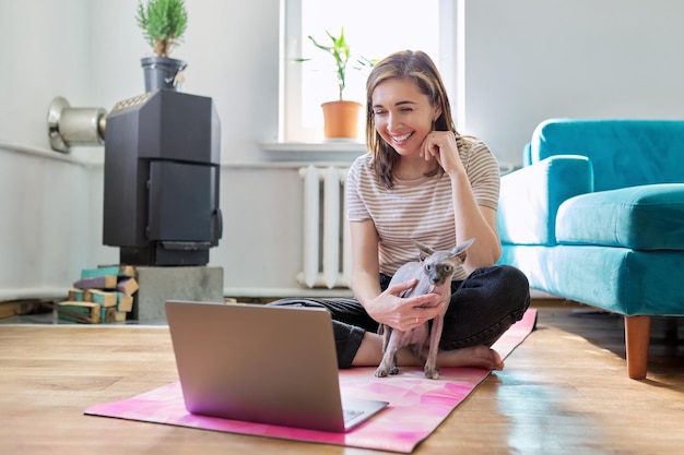 Middleaged smiling woman with laptop and cat on the floor