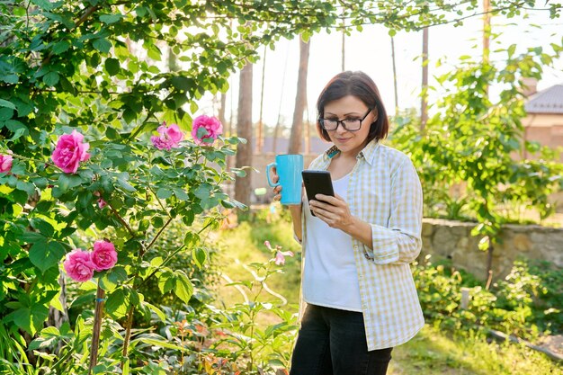 Middleaged woman relaxing in garden with smartphone and cup in her hands