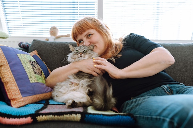 Middleaged woman sits on sofa by window with cat