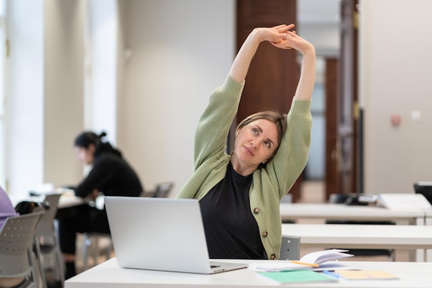 Middleaged woman student warming up body and muscles at classroom feeling satisfied with work done