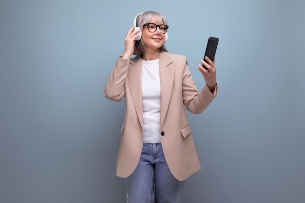 Middleaged woman in a stylish jacket listens to music in large headphones on a bright background